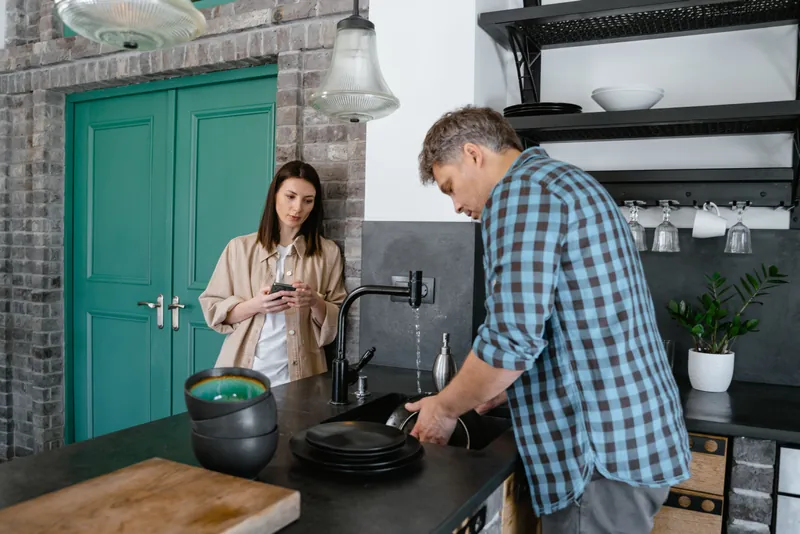 Husband doing the dishes while the wife criticizes his effort