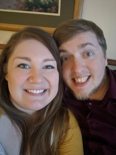 Jake and Melissa sitting on a couch, cheek to cheek smiling