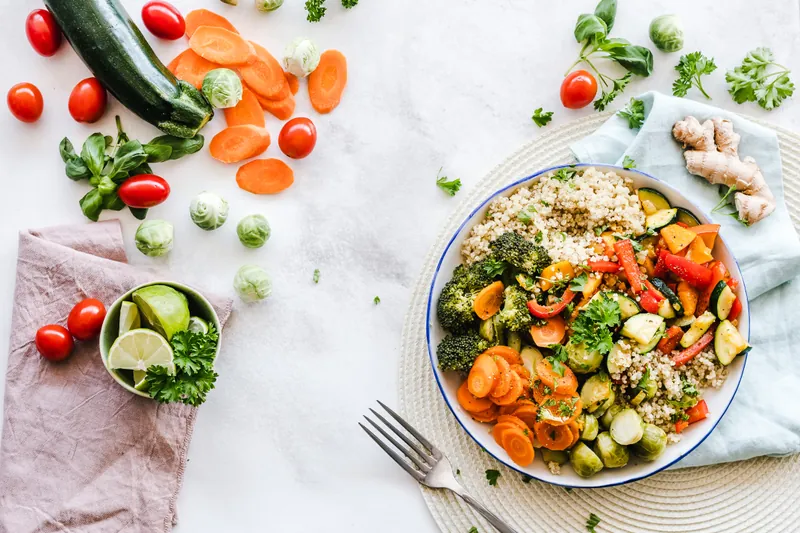Quinoa bowl with colorful veggies placed on a table with veggies scattered around it