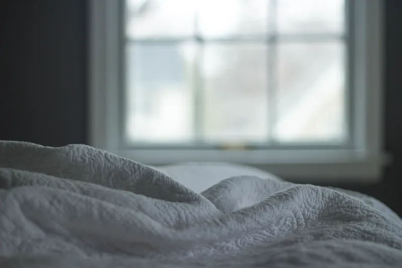 Ruffled white sheets on a bed facing a window